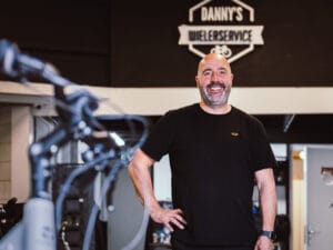 Portret van een lachende fietsenmaker in zijn werkplaats bij Danny’s Wielerservice.