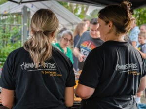 Twee medewerkers van een frietwagen bereiden eten terwijl bezoekers wachten tijdens een zomers buurtfeest.